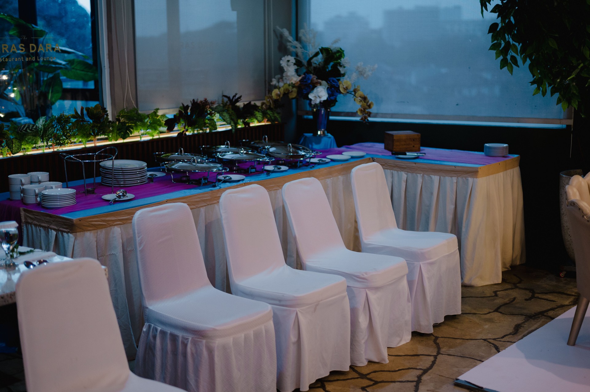 Elegant dinner reception setup with white chairs and a buffet table in a banquet hall